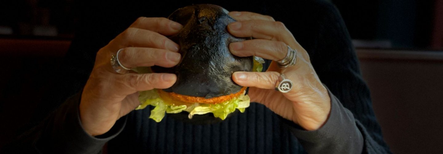 mani con anelli che afferrando panino al carbone con Burger e insalata