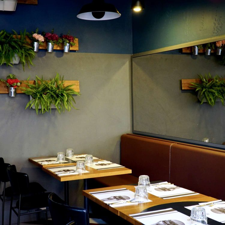 sala interna ristorante con tavoli in legno, tovagliette di carta, specchio su una parete e piante e fiori sull'altra parete